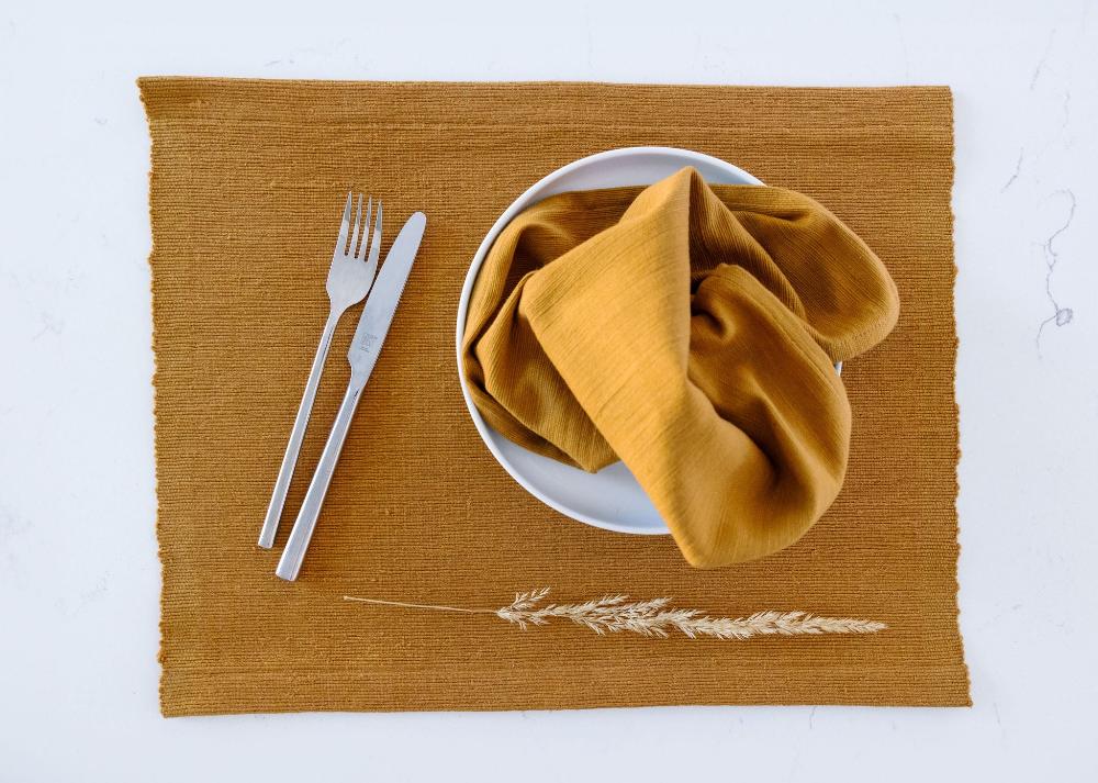 Semien cocktail napkin and placemat in bronze on a white background with cutlery and a plate