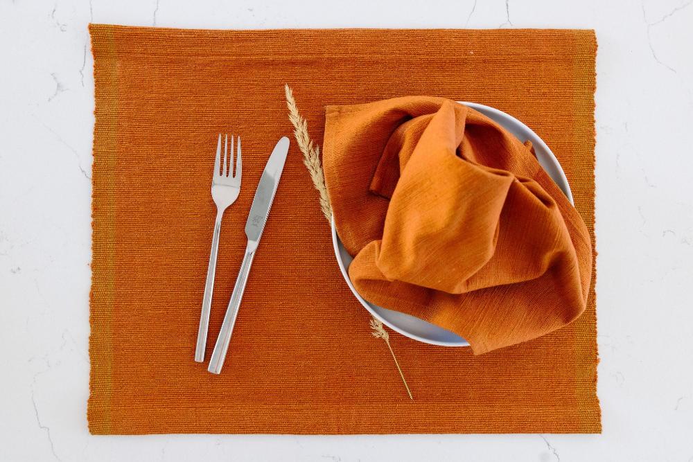 Semien cocktail napkin and placemat in copper on a white background with cutlery and a plate
