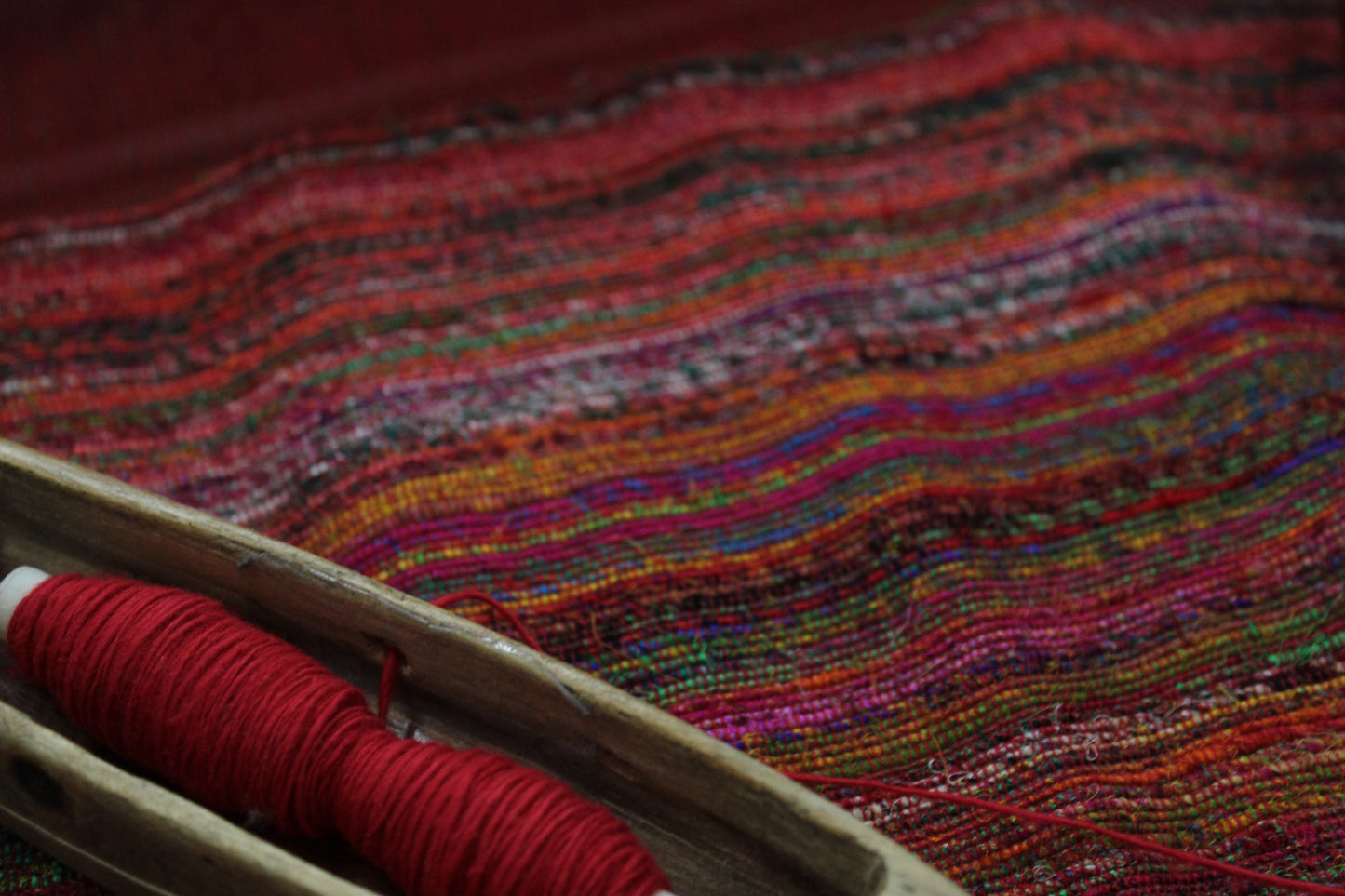 Close-up of harar fabric with a spool of red thread on a wooden surface.