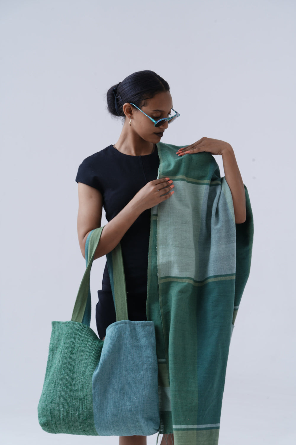 Ethiopian model holding borsa bag with mareb towel in teal hanging on shoulder against white background