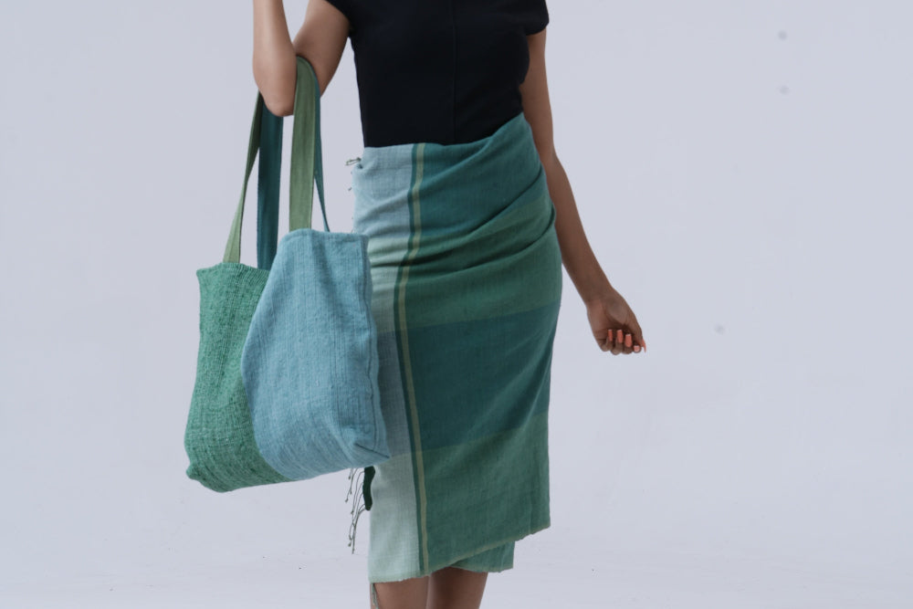 Ethiopian model holding borsa tote bag in teal with mareb towel in teal wrapped around her waist againt white background