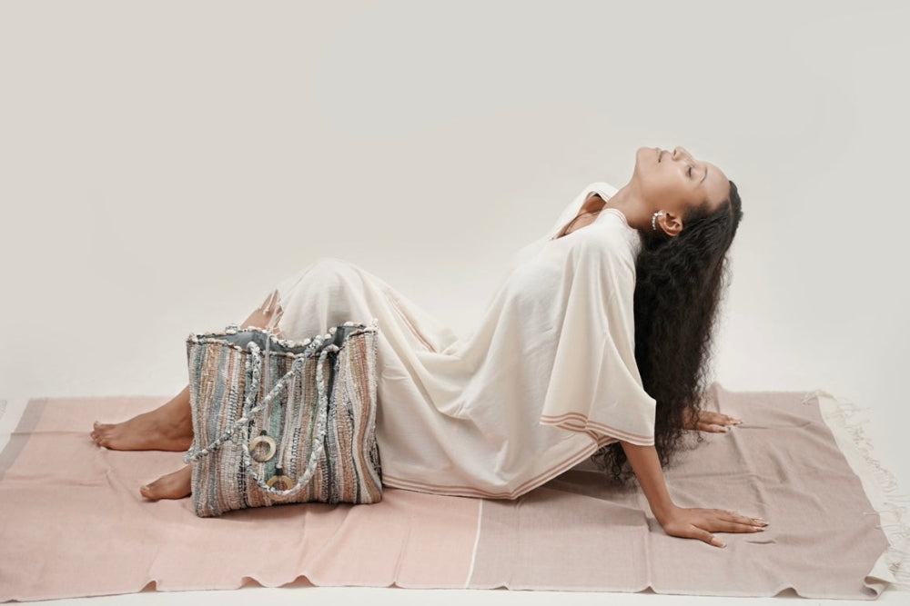 Ethiopian model_laying on abay blush towel wearing petra kaftan with a fasika bag beside