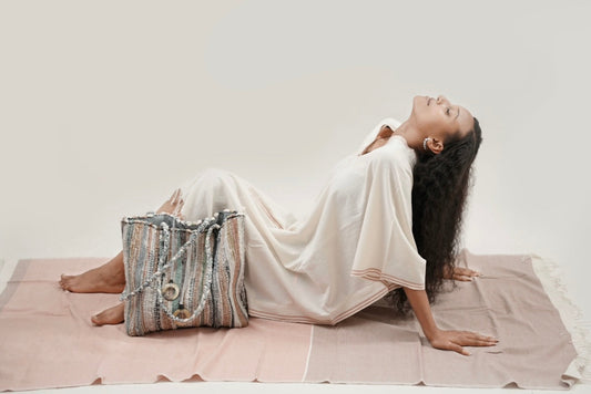Ethiopian model_laying on abay blush towel wearing petra kaftan with a fasika bag beside