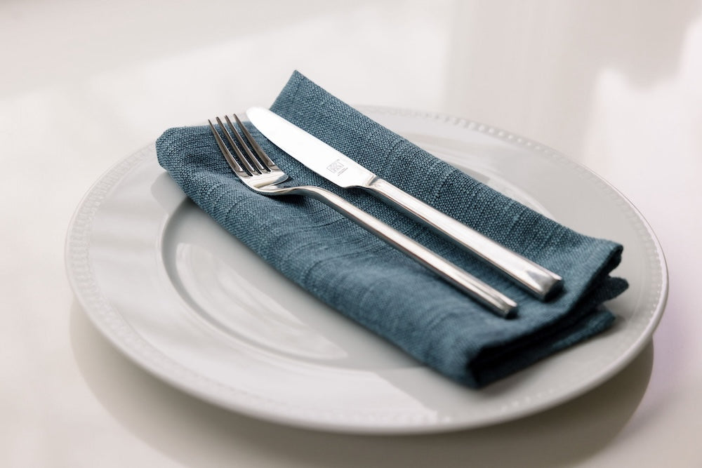 Semien cocktail napkin folded on a plate with a fork and knife