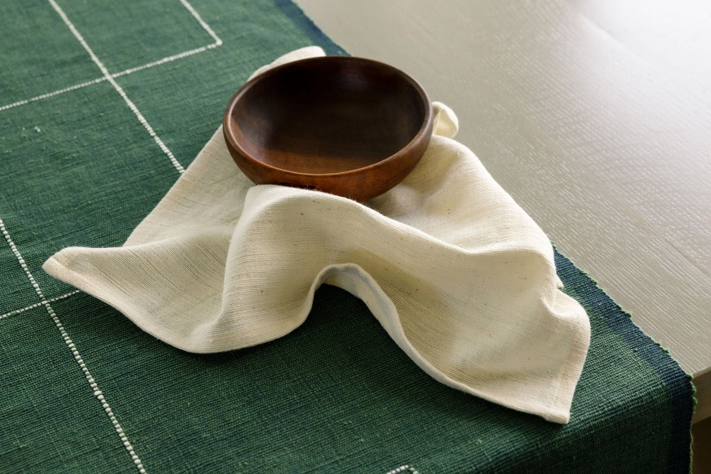 Ivory Semien cocktail napkin with a wooden bowl and cedar table runner