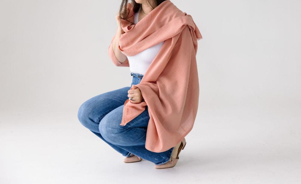 Female model squatting while wearing Maraki shawl in blush