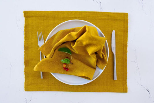 Semien cocktail napkin and placemat in gold on a white background with cutlery and a plate