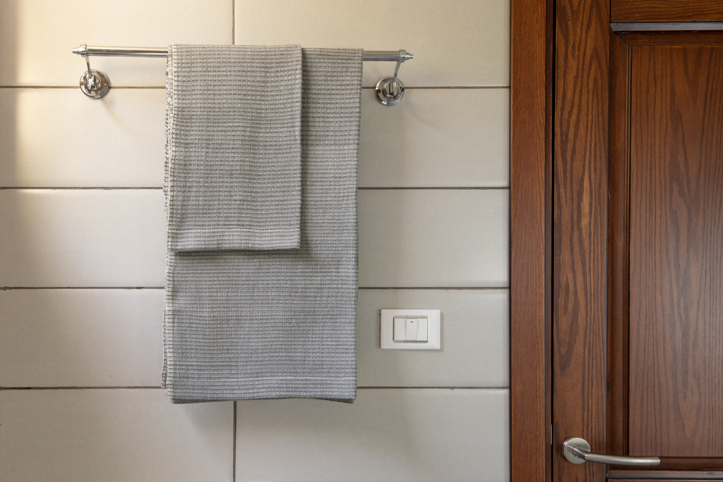 Handwoven bath towel in light grey, displayed in a bathroom setting, with a wooden cabinet and towel rack.