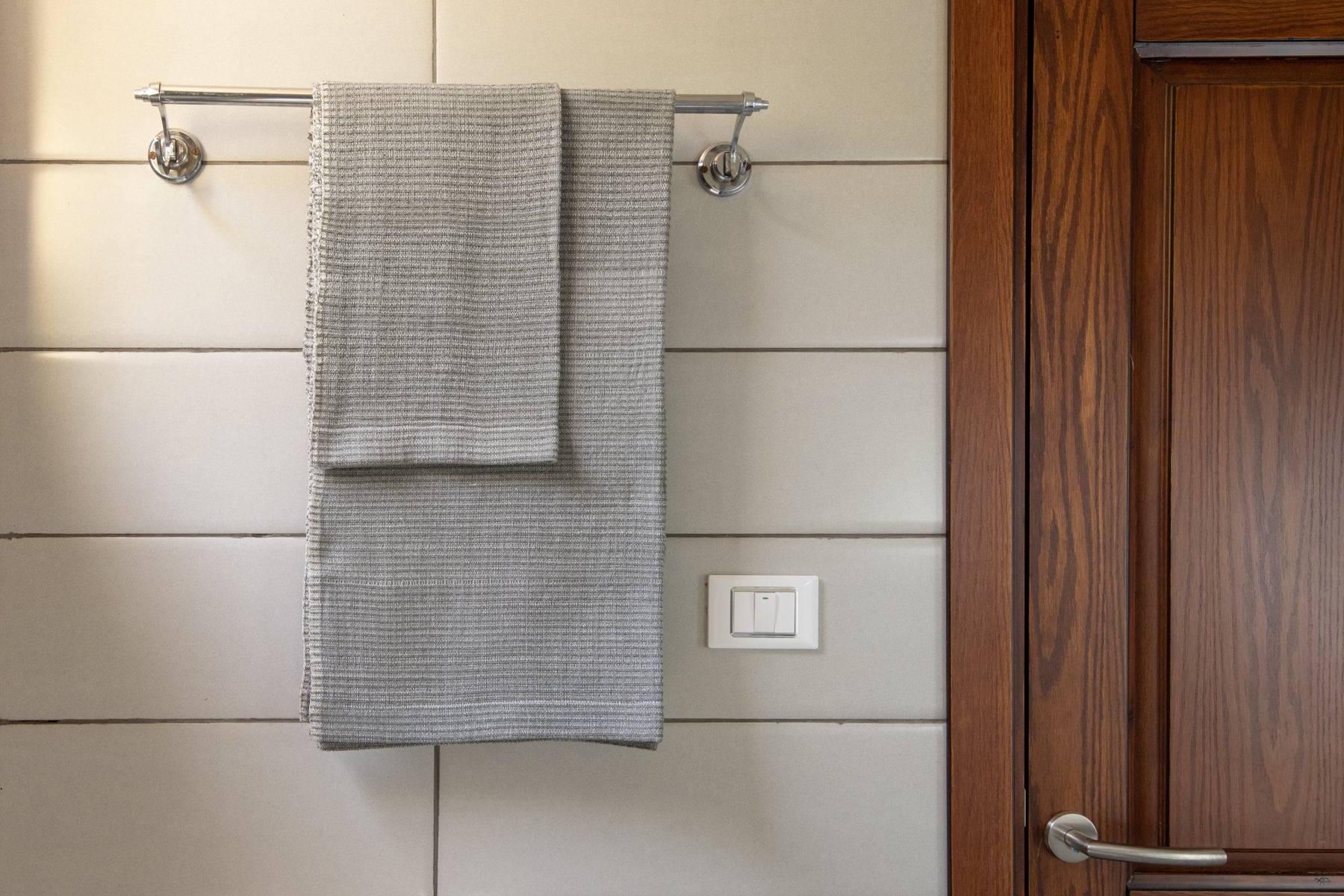 Handwoven bath towel in light grey, displayed in a bathroom setting, with a wooden cabinet and towel rack.