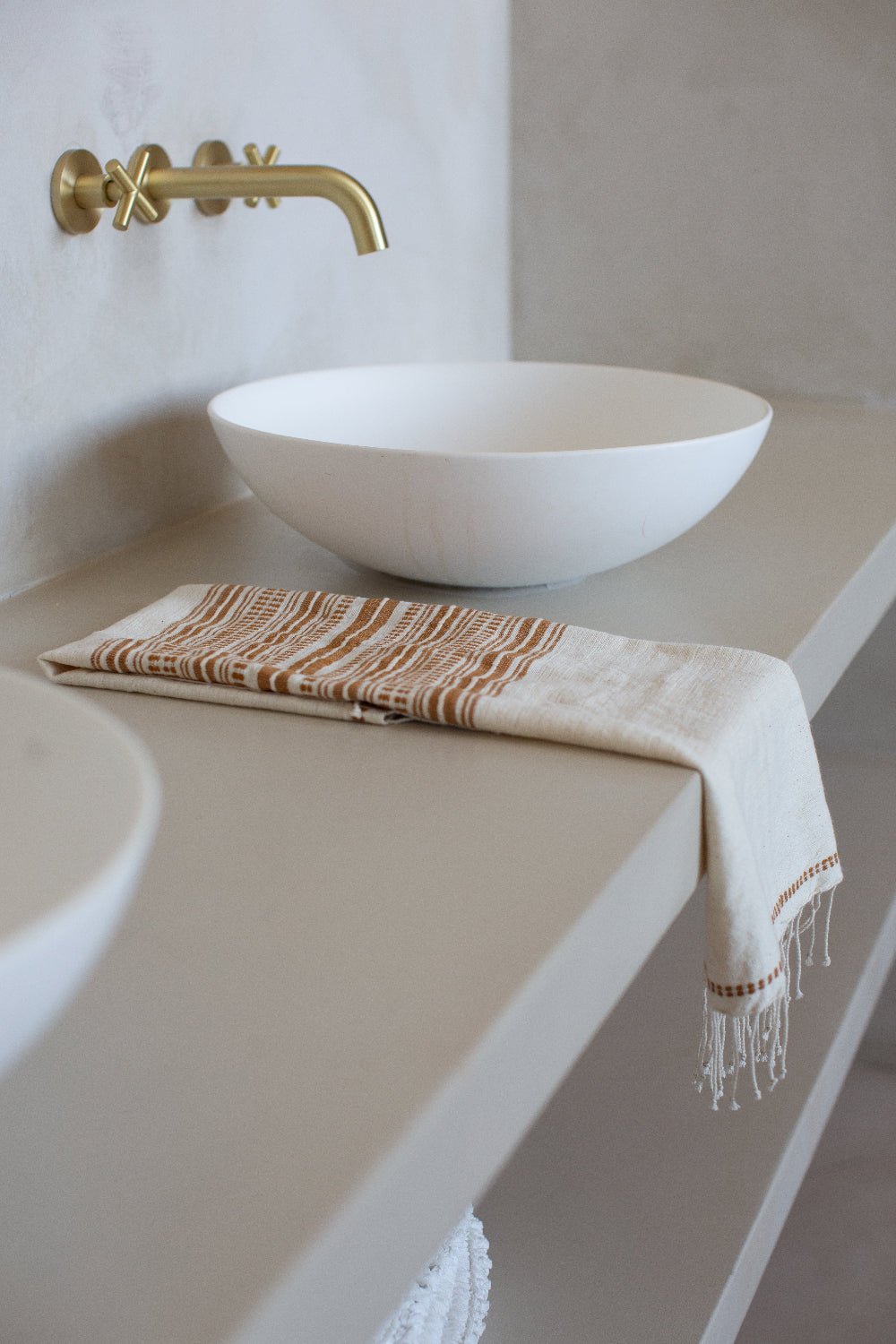 genale hand towel in bronze on light grey countertop with white ceramic sink with gold faucet