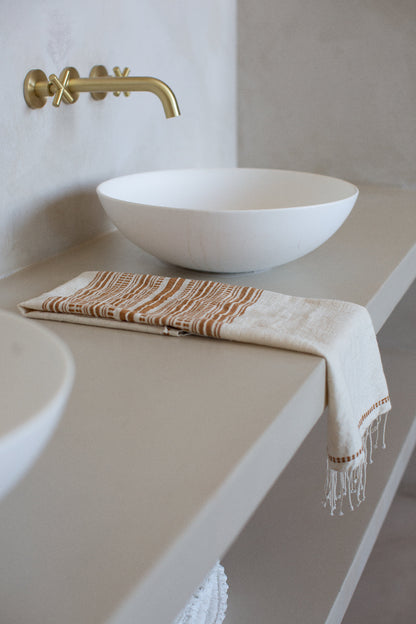 genale hand towel in bronze on light grey countertop with white ceramic sink with gold faucet