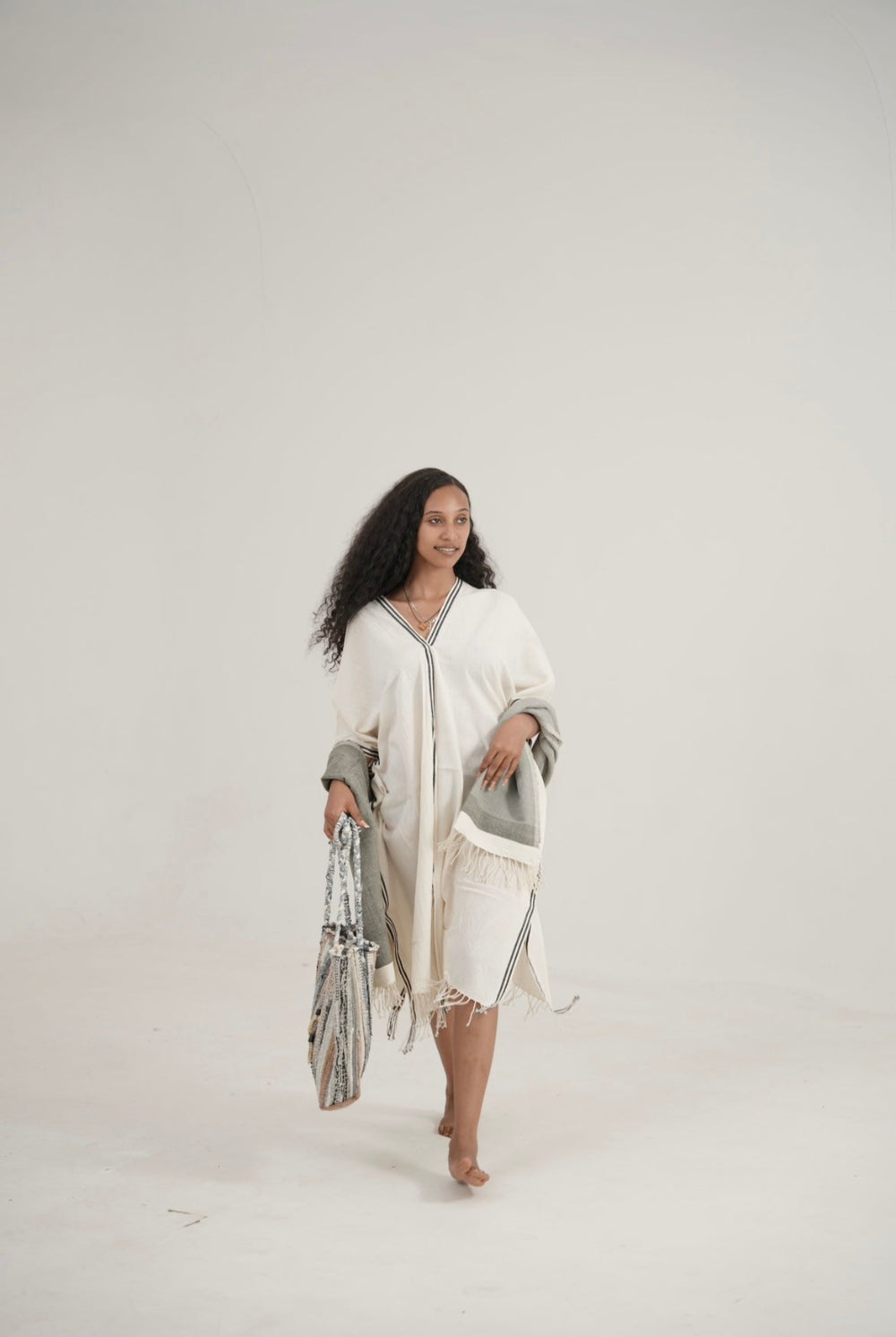 model wearing petra kaftan with abay towel in grey holding fasika bag