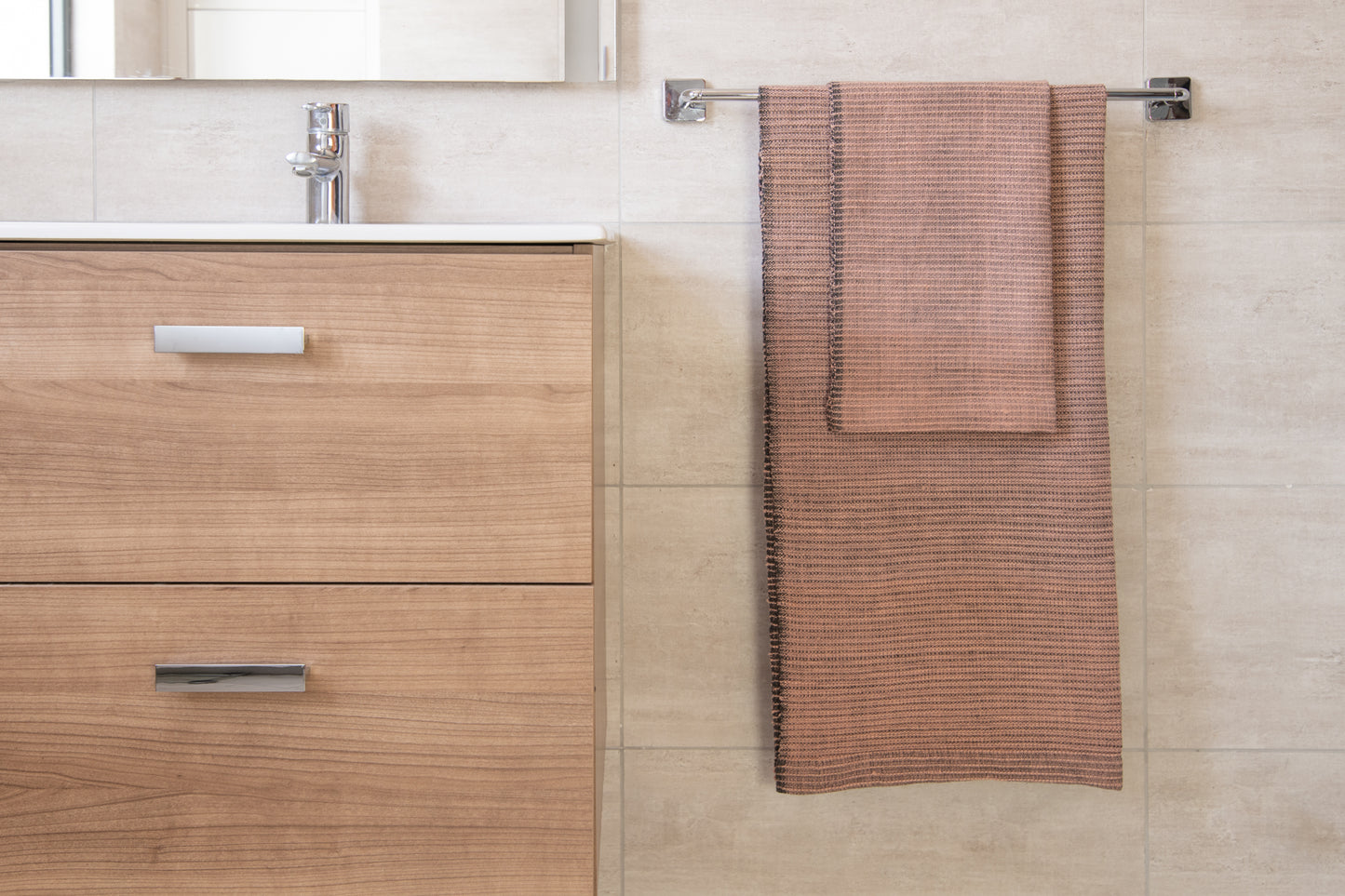 Handwoven bath towel in blush, displayed in a bathroom setting, with a wooden cabinet and towel rack.