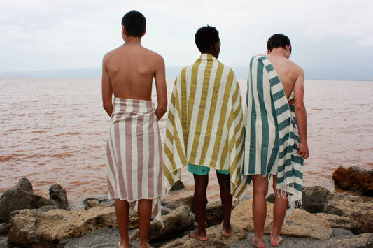 Omo towel beach towel in clay, moss, teal with three male models at the beach